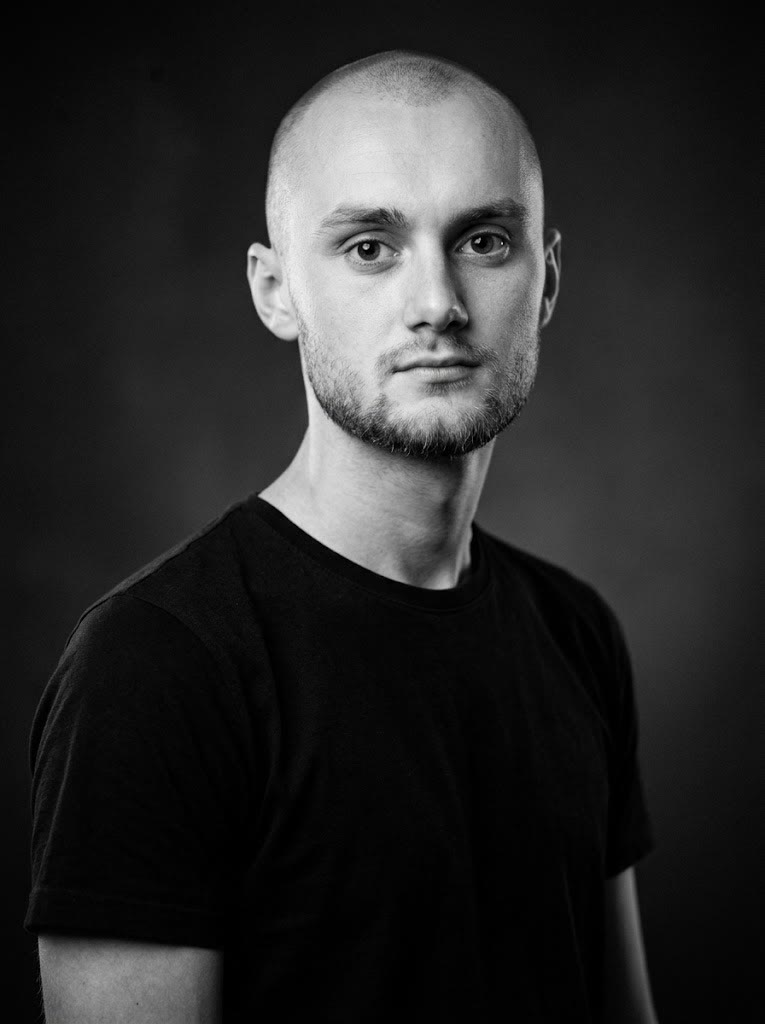 Portrait en noir et blanc d’Amaury Decloux, en t-shirt noir sur fond sombre.